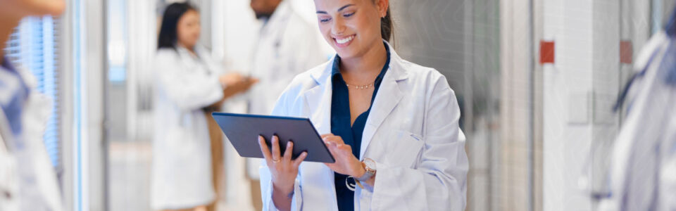 healthcare professionals speak while a woman in a lab coat uses contract management software for healthcare on a tablet