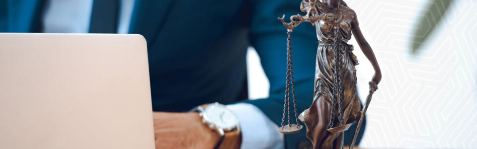 Cropped shot of lady justice statue on table and lawyer using contract management software for legal departments on computer