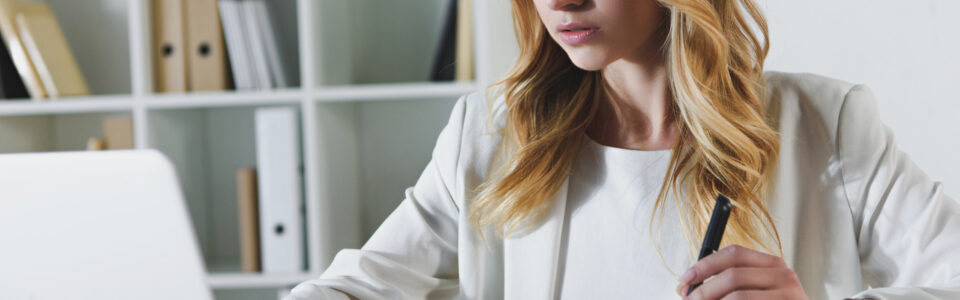 woman sitting at desk looking at laptop computer holding pen near contract learning how AI contract operations enhances business continuity