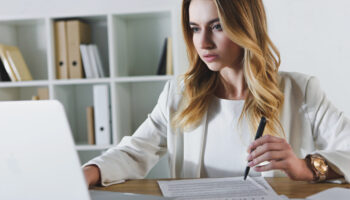 woman sitting at desk looking at laptop computer holding pen near contract learning how AI contract operations enhances business continuity