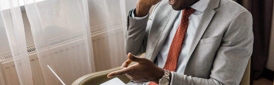 smiling businessman talking on smartphone and pointing at laptop while using contract management automation