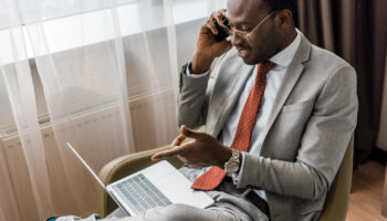 smiling businessman talking on smartphone and pointing at laptop while using contract management automation