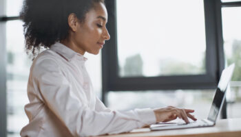 side view of woman sitting at desk using laptop computer to learn about contract management workflows