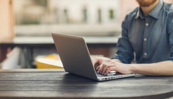 A man sits at a table, using his laptop to leverage contract management software for a smooth and efficient negotiation process