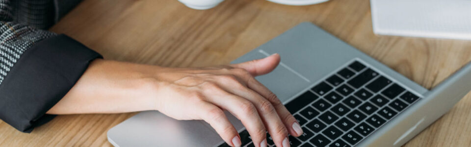 cropped image of business woman holding a cup of coffee and using a digital contract automation tool on her laptop computer in office