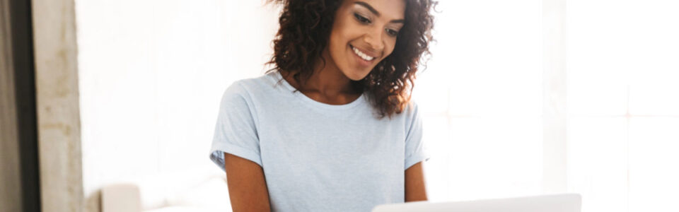 smiling woman sits at desk and uses computer to learn about the best contract database software